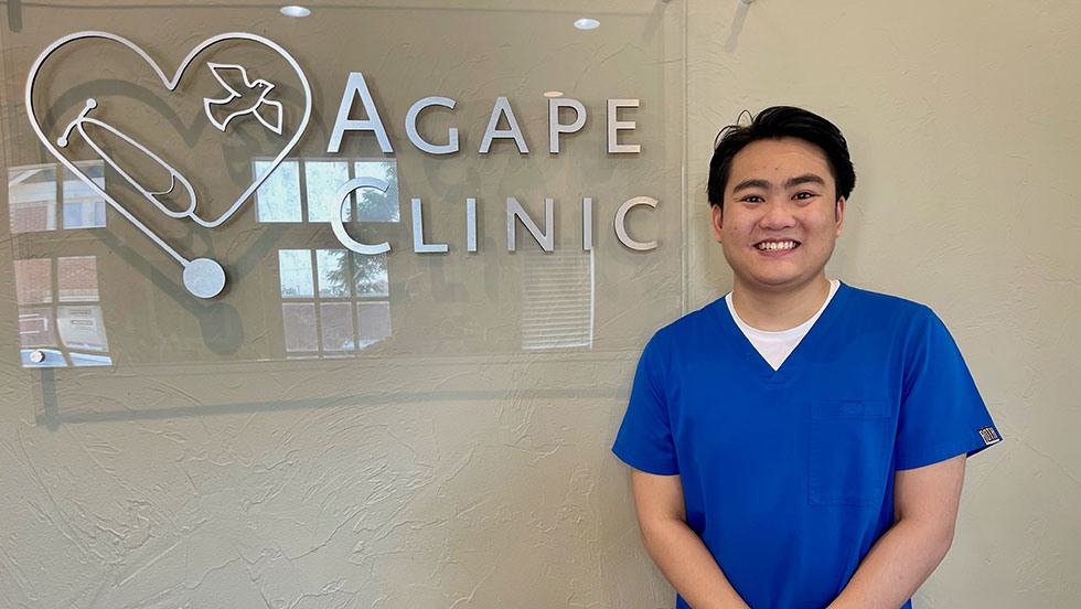 Photo of smiling student in front of Agape Clinic sign